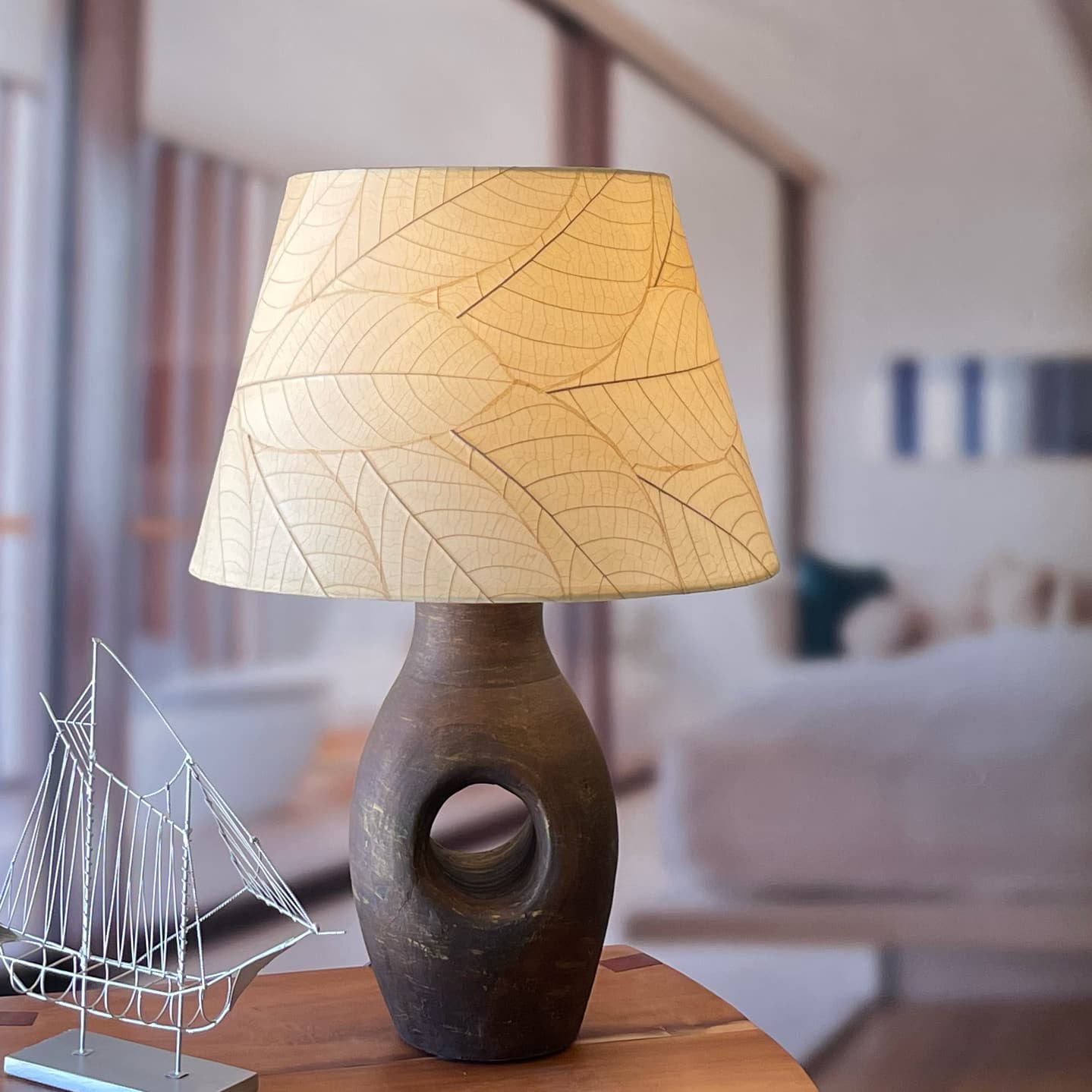 In a softly lit reading nook, crafted by the artisans of Eangee Home Design, the 18 Inch British Empire Shade in natural stands gracefully, featuring fossilized cocoa leaf shade, wrought iron frame, eco friendly, sustainably sourced, adding warmth and character to the space.