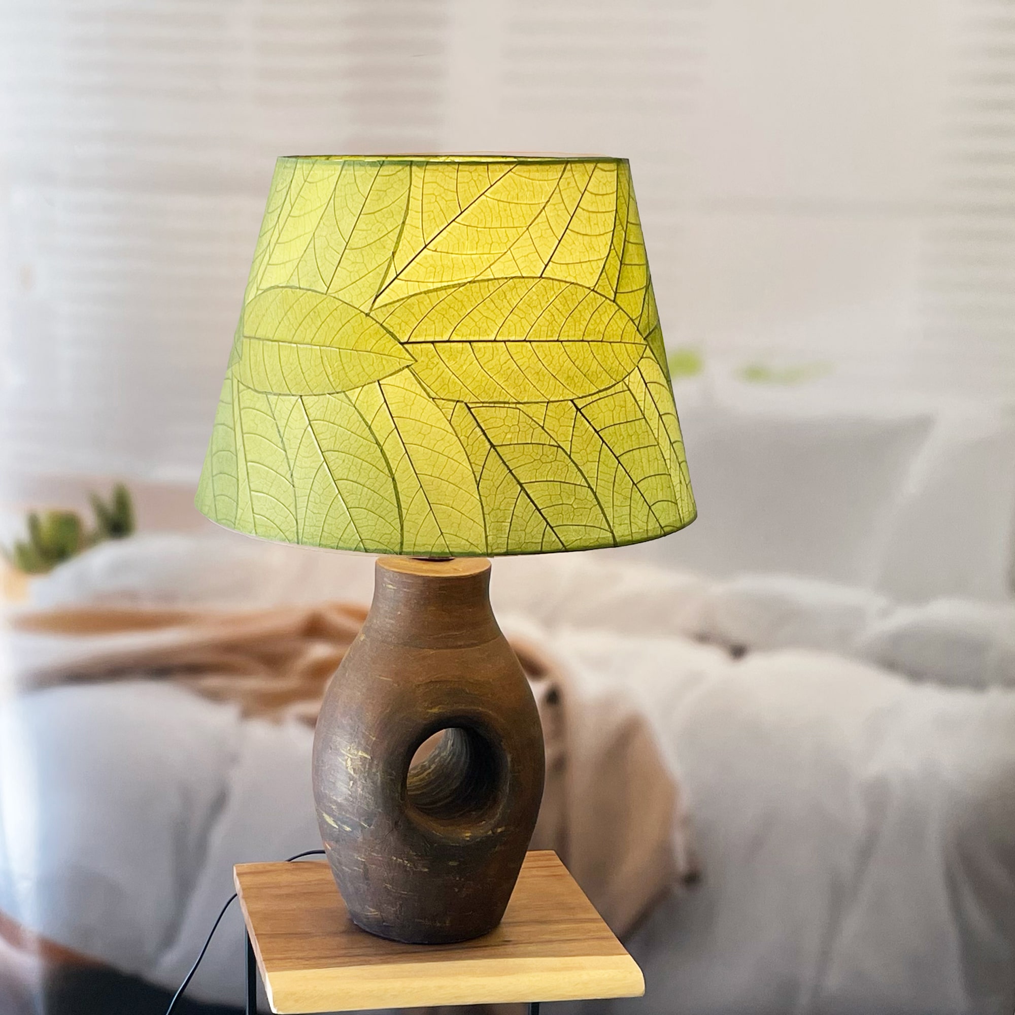 In a coastal inspired living room, crafted by the artisans of Eangee Home Design, the 16 Inch British Empire Shade Green Color in  stands gracefully, featuring fossilized cocoa leaf shade, wrought iron frame, fair trade, eco friendly, sustainably sourced, adding warmth and character to the space.