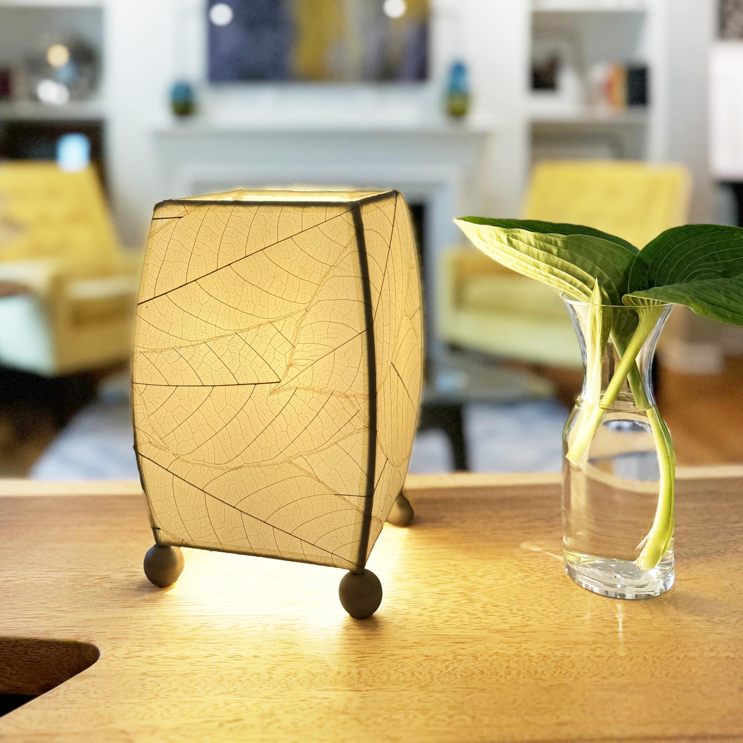 In a coastal inspired living room, crafted by the artisans of Eangee Home Design, the Mini Square Cocoa Leaf Table Lamp in natural stands gracefully, featuring fossilized cocoa leaf shade, wrought iron frame, fair trade, eco friendly, sustainably sourced, handcrafted, adding warmth and character to the space.