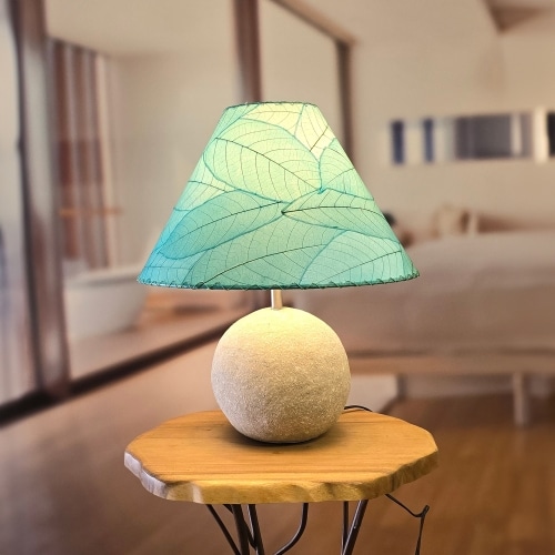 In a softly lit reading nook, crafted by the artisans of Eangee Home Design, the Bell Shade Cocoa in sea blue stands gracefully, featuring fossilized cocoa leaf shade, wrought iron frame, handcrafted, adding warmth and character to the space.