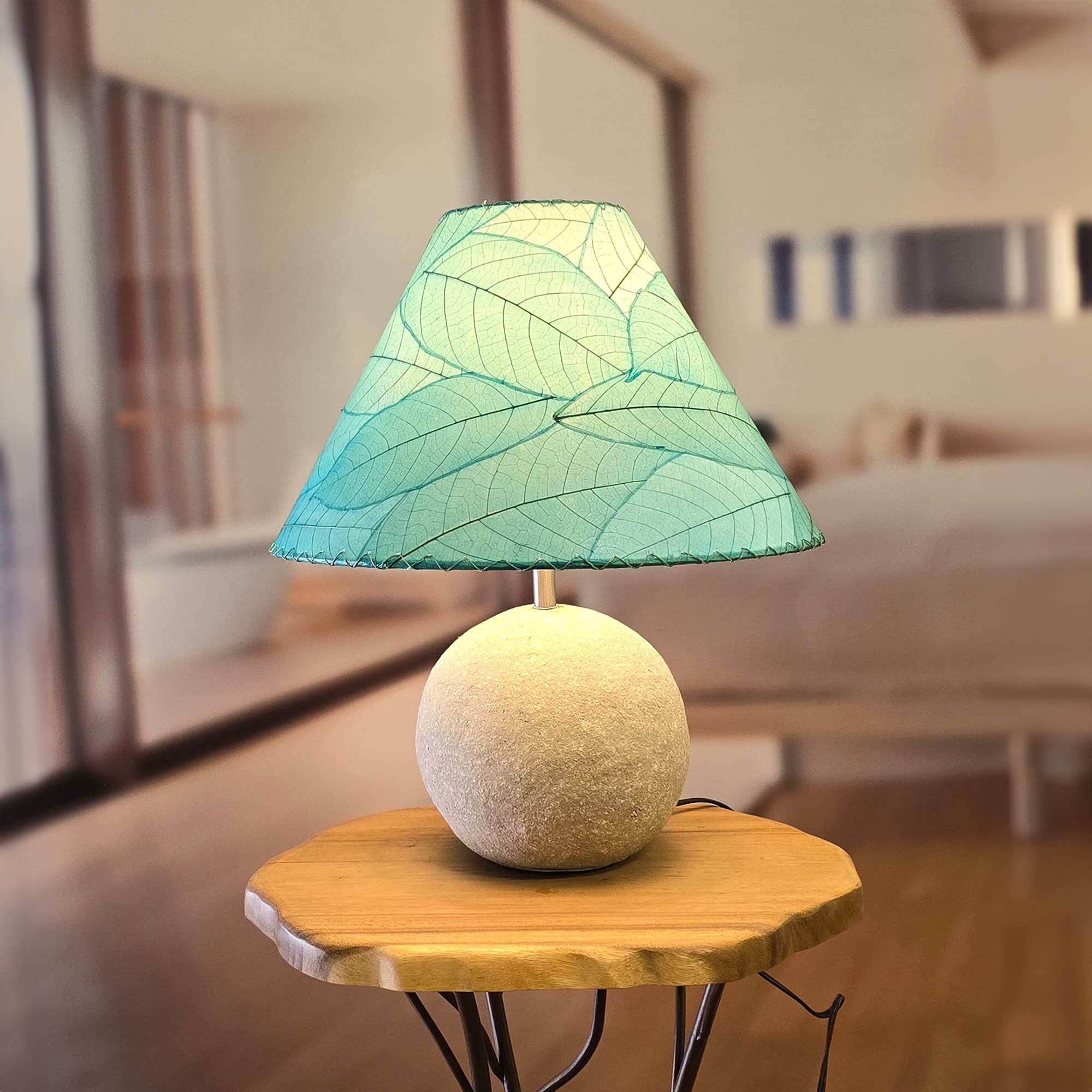 In a softly lit reading nook, crafted by the artisans of Eangee Home Design, the Bell Shade Cocoa in sea blue stands gracefully, featuring fossilized cocoa leaf shade, wrought iron frame, handcrafted, adding warmth and character to the space.