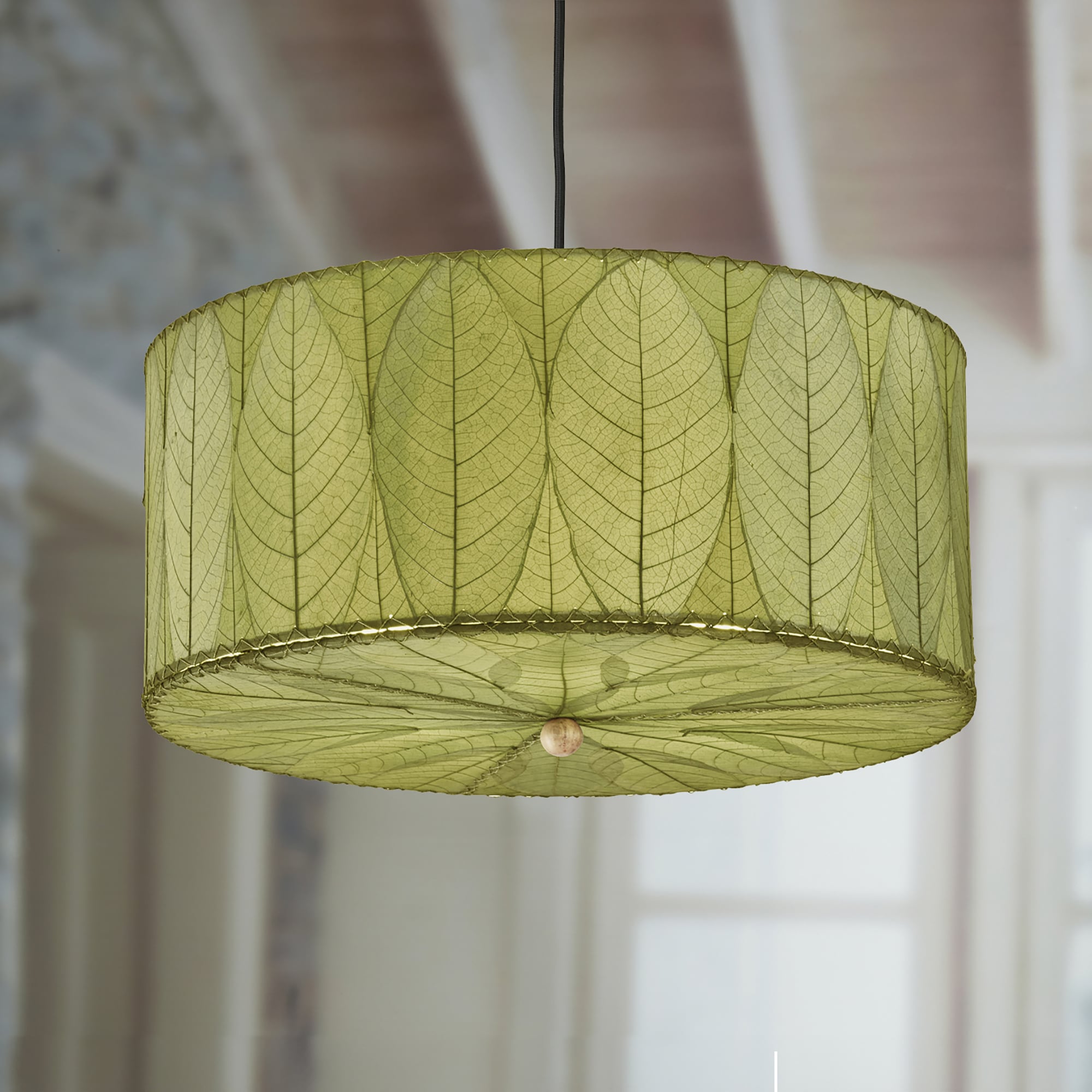 In a coastal inspired living room, a green lamp crafted by the artisans of Eangee Home Design called the Drum Pendant 24 Inch stands gracefully, featuring handcrafted detailing, sustainably sourced, handcrafted, adding warmth and character to the scene.