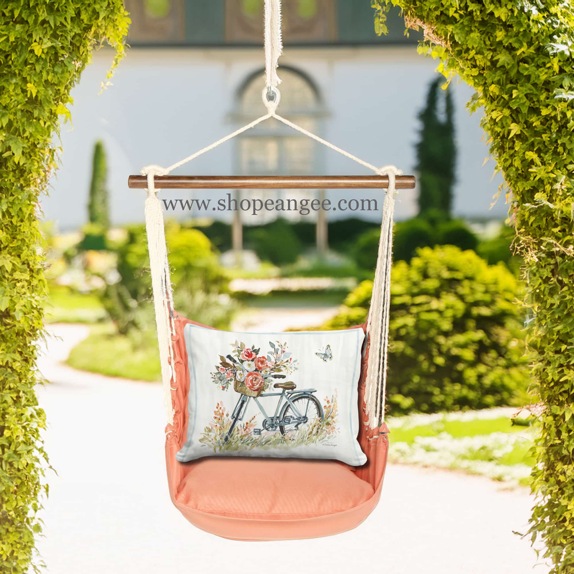 In a shaded porch swing a multi colored outdoor swing crafted by the artisans of Magnolia Casual called the Swing Set 4 piece Living Coral w/ Bike with Flower Basket is displayed featuring 100 percent weather resistant fabric, weather resistant polyester fabric, handcrafted adding comfort and style to the space featuring with a coral motif and shades of coral.