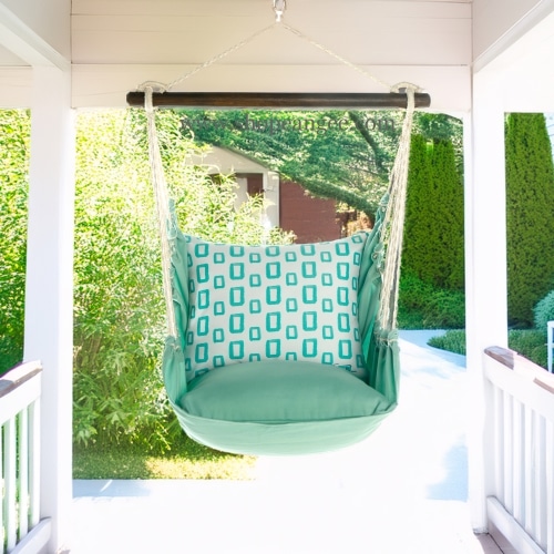 In a cozy garden seating area a green outdoor swing crafted by the artisans of Magnolia Casual called the Swing Set 4 piece Seafoam Green Solid w/ Infinite Frames is displayed featuring 100 percent weather resistant fabric, weather resistant polyester fabric, handcrafted adding comfort and style to the space featuring shades of green.