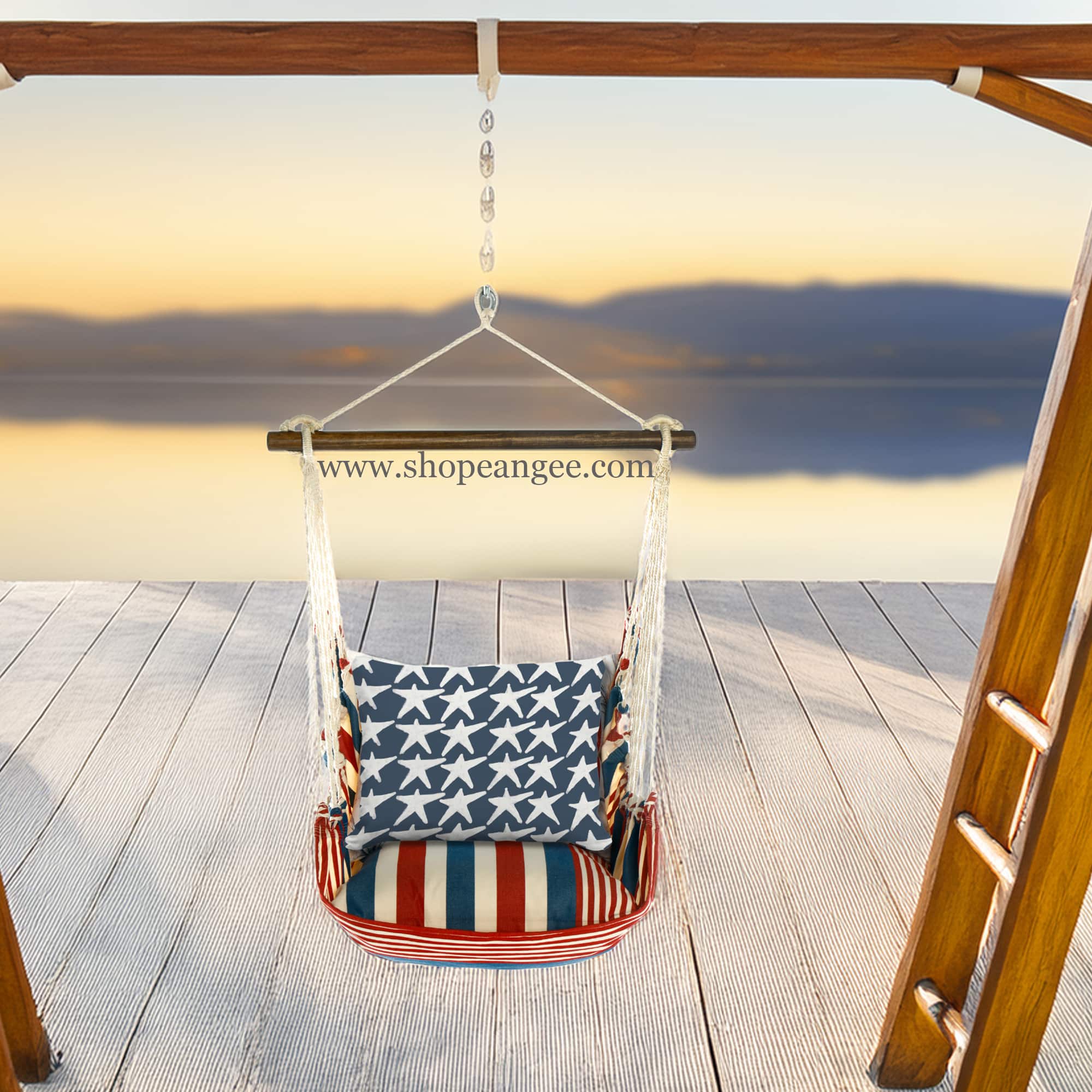 In a poolside chaise a multi colored outdoor swing crafted by the artisans of Magnolia Casual called the Swing Set 4 piece Stars & Stripes w/ Flag Stars is displayed featuring 100 percent weather resistant fabric, weather resistant polyester fabric, handcrafted adding comfort and style to the space featuring with a stripes motif.