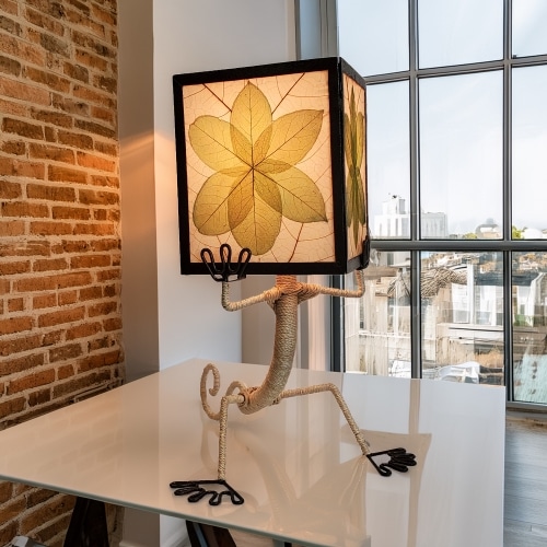 Gecko?shaped table lamp crafted by Eangee Home Design with green fossilized cocoa?leaf panels hand?stitched onto a wrought?iron frame; playful gecko silhouette hugs the shade, and gentle light filters through every vein; fair?trade craftsmanship using sustainable resources