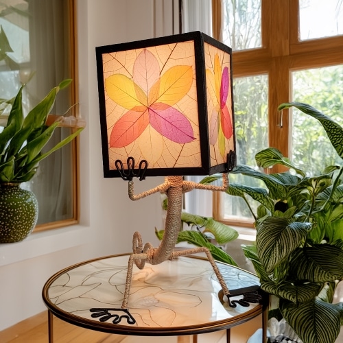 Gecko?shaped table lamp crafted by Eangee Home Design with multi color fossilized cocoa?leaf panels hand?stitched onto a wrought?iron frame; playful gecko silhouette hugs the shade, and radiant light shines against the leaf?veined surface; fair?trade craftsmanship using sustainable resources