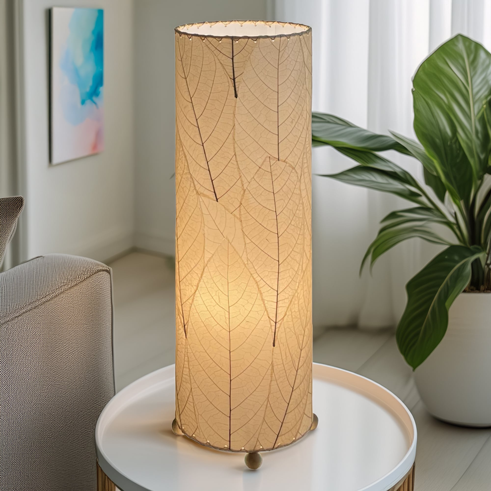 In a sun drenched entryway, crafted by the artisans of Eangee Home Design, the 24 Inch Cocoa Leaf Cylinder Table Lamp in natural stands gracefully, featuring fossilized cocoa leaf shade, fair trade, eco friendly, sustainably sourced, handcrafted, adding warmth and character to the space.