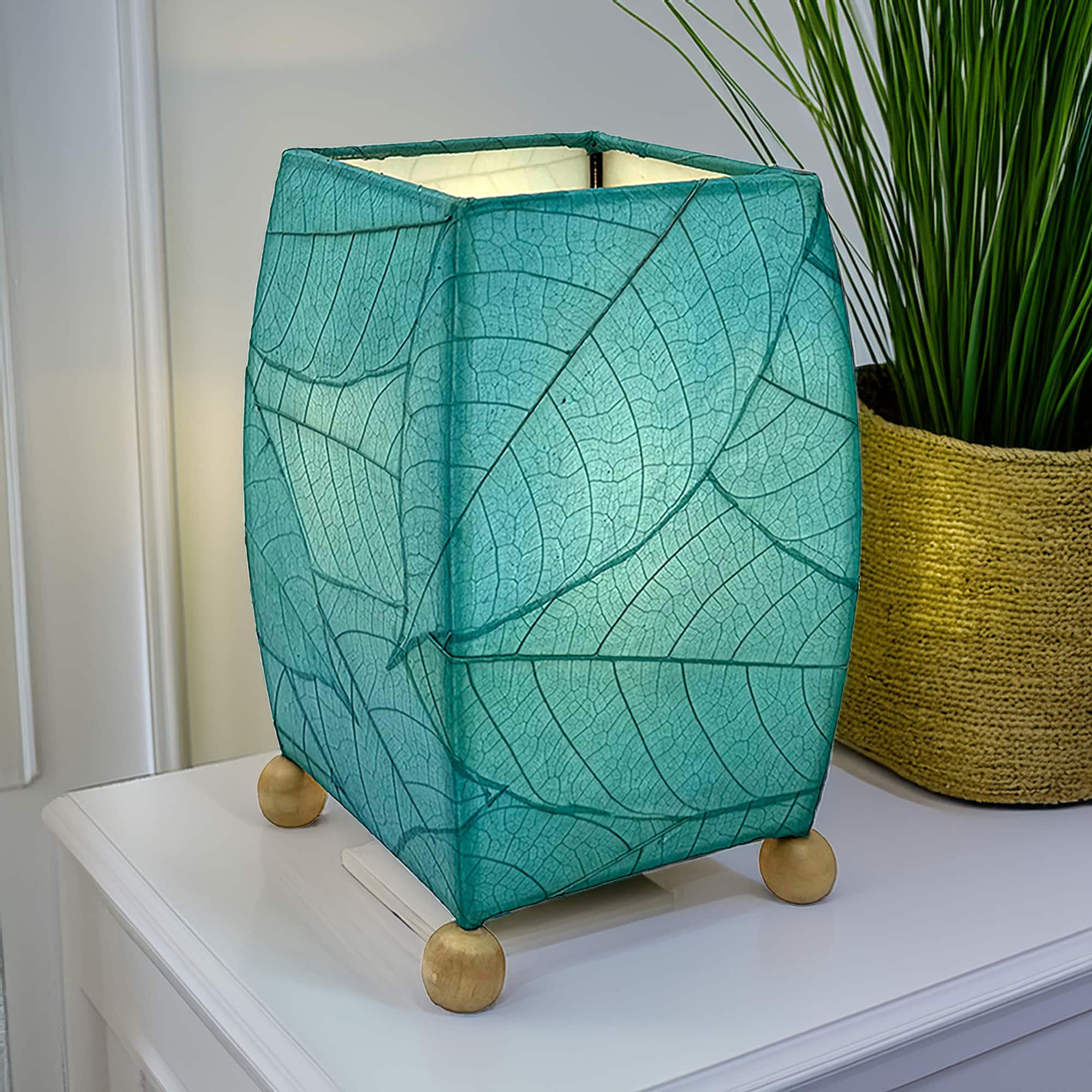 In a minimalist loft with natural textures, crafted by the artisans of Eangee Home Design, the Mini Square Cocoa Leaf Table Lamp in sea blue stands gracefully, featuring fossilized cocoa leaf shade, wrought iron frame, fair trade, eco friendly, sustainably sourced, handcrafted, adding warmth and character to the space.
