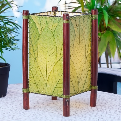 In a sun drenched entryway, crafted by the artisans of Eangee Home Design, the Fortune Table Lamp in green stands gracefully, featuring fossilized cocoa leaf shade, abaca rope accents, rattan leg supports, adding warmth and character to the space.