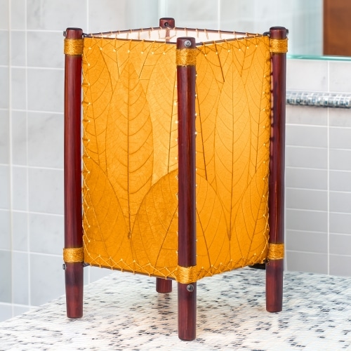 Square Fortune series table lamp crafted by Eangee Home Design wrapped in orange fossilized cocoa leaves, abaca?stitched edges, rattan legs; geometric lines softened as cozy light spills across the textured leaf panels; sustainably handcrafted by skilled artisans