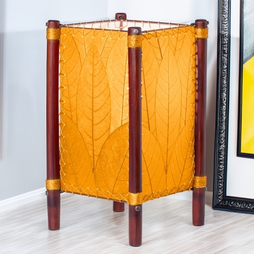Crafted by the artisans of Eangee Home Design, the Fortune Table Lamp in orange against a clean backdrop, featuring fossilized cocoa leaf shade, abaca rope accents, rattan leg supports.