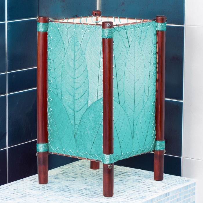In a modern interior with earth tones, crafted by the artisans of Eangee Home Design, the Fortune Table Lamp in sea blue stands gracefully, featuring fossilized cocoa leaf shade, abaca rope accents, rattan leg supports, adding warmth and character to the space.