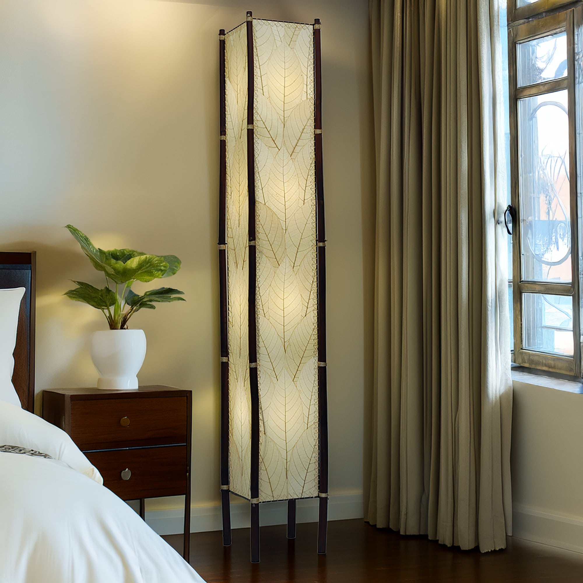 In a sunlit corner of a loft, the Fortune Giant Floor crafted by the artisans of Eangee Home Design Lamp in natural finish by Eangee Home Design stands beside a rattan side table, its fossilized cocoa leaf panels, abaca twine accents, rattan legs, powder coated wrought iron frame, wrought iron frame, hand placed natural leaves, hand placed leaf panels, and abaca twine stitching casting a warm glow that some pieces don't just fill a space they define it.