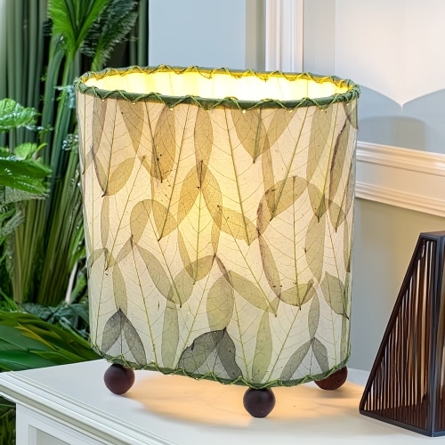 In a sun drenched entryway, crafted by the artisans of Eangee Home Design, the Mini Guyabano Table Lamp in green stands gracefully, featuring fossilized cocoa leaf shade, guyabano leaf shade, wrought iron frame, adding warmth and character to the space.