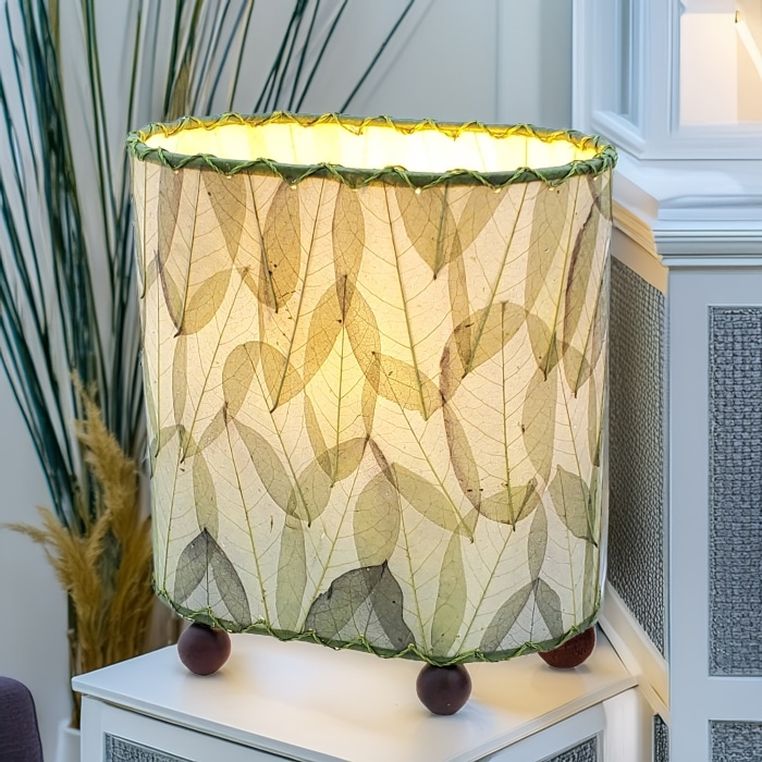 Crafted by the artisans of Eangee Home Design, the Mini Guyabano Table Lamp in green against a clean backdrop, featuring fossilized cocoa leaf shade, guyabano leaf shade, wrought iron frame.
