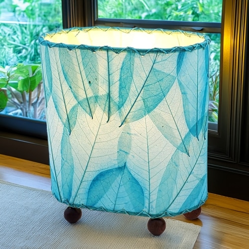 In a sun drenched entryway, crafted by the artisans of Eangee Home Design, the Mini Guyabano Table Lamp in sea blue stands gracefully, featuring fossilized cocoa leaf shade, guyabano leaf shade, wrought iron frame, adding warmth and character to the space.