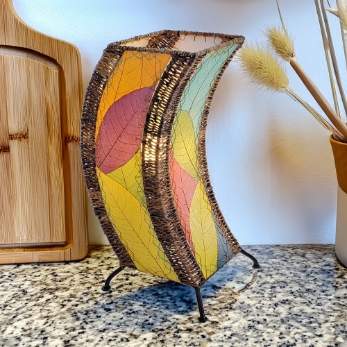 In a modern interior with earth tones, crafted by the artisans of Eangee Home Design, the C Shape Table Lamp in multi color stands gracefully, featuring fossilized cocoa leaf shade, abaca rope accents, fair trade, handcrafted, adding warmth and character to the space.