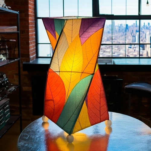 In a sun drenched entryway, crafted by the artisans of Eangee Home Design, the Twist Table Lamp in multi color stands gracefully, featuring fossilized cocoa leaf shade, wrought iron frame, handcrafted, adding warmth and character to the space.