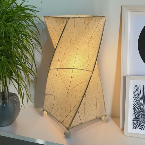 In a sun drenched entryway, crafted by the artisans of Eangee Home Design, the Twist Table Lamp in natural stands gracefully, featuring fossilized cocoa leaf shade, wrought iron frame, handcrafted, adding warmth and character to the space.