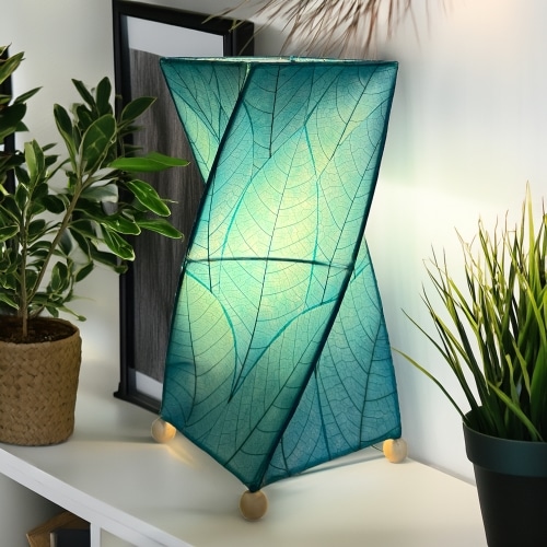 In a coastal inspired living room, crafted by the artisans of Eangee Home Design, the Twist Table Lamp in sea blue stands gracefully, featuring fossilized cocoa leaf shade, wrought iron frame, handcrafted, adding warmth and character to the space.