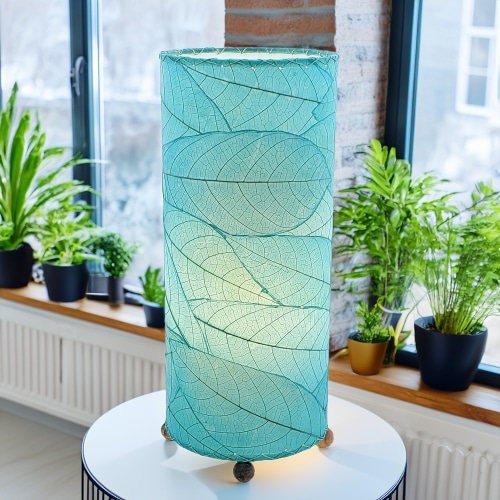 In a modern interior with earth tones, crafted by the artisans of Eangee Home Design, the Cocoa Leaf Cylinder Table Lamp in sea blue stands gracefully, featuring fossilized cocoa leaf shade, wrought iron frame, handcrafted, adding warmth and character to the space.