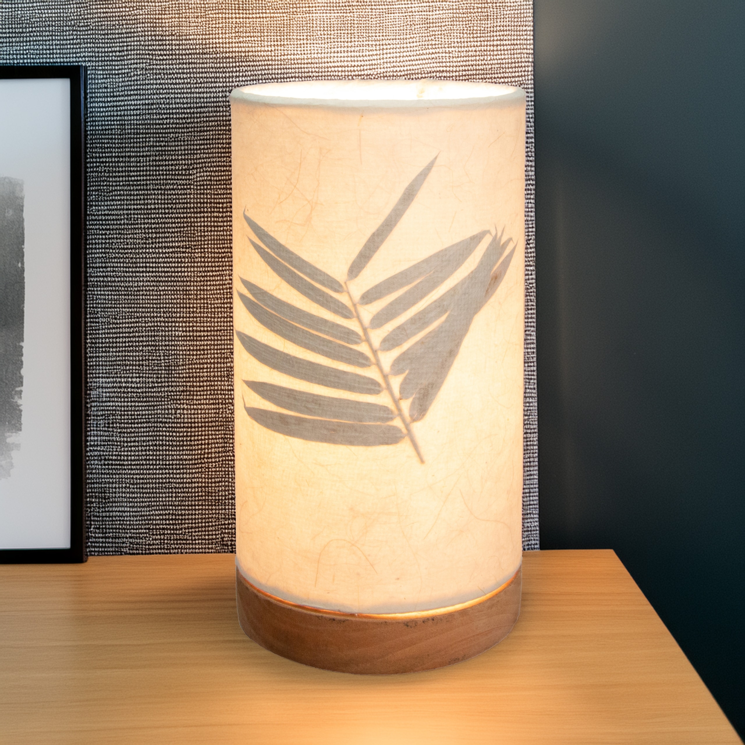 In a sun drenched entryway, crafted by the artisans of Eangee Home Design, the Mini Paper Cylinder Table Lamp Bamboo in natural stands gracefully, featuring reclaimed mango wood base, recycled paper shade, sustainably sourced, recycled materials, adding warmth and character to the space.