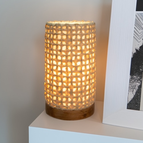 In a quiet bedside corner, crafted by the artisans of Eangee Home Design, the Mini Paper Cylinder Table Lamp Mesh in natural stands gracefully, featuring reclaimed mango wood base, recycled paper shade, sustainably sourced, recycled materials, adding warmth and character to the space.
