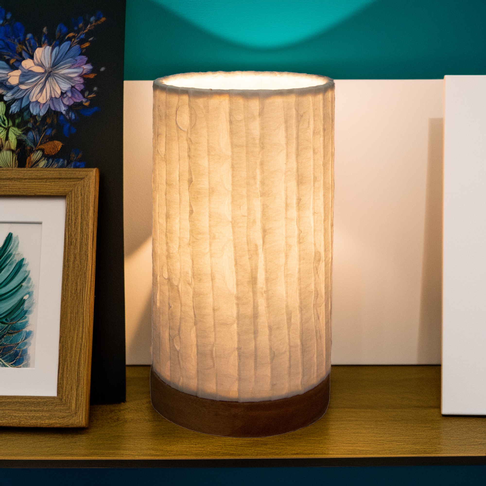 In a softly lit reading nook, crafted by the artisans of Eangee Home Design, the Mini Paper Cylinder Table Lamp Lines in natural stands gracefully, featuring reclaimed mango wood base, recycled paper shade, sustainably sourced, recycled materials, adding warmth and character to the space.
