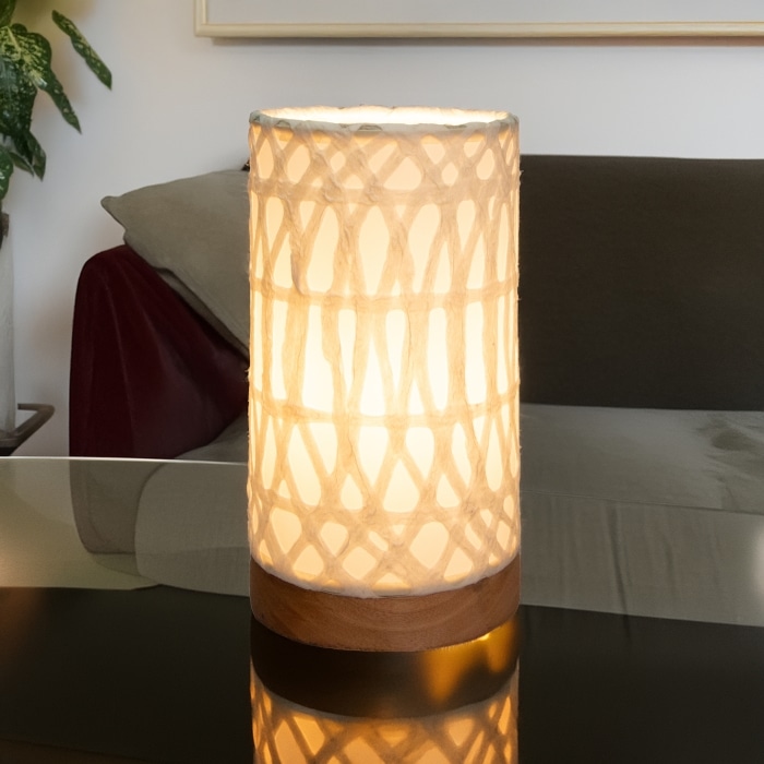 In a coastal inspired living room, crafted by the artisans of Eangee Home Design, the Mini Paper Cylinder Table Lamp Arches in natural stands gracefully, featuring reclaimed mango wood base, recycled paper shade, sustainably sourced, recycled materials, adding warmth and character to the space.