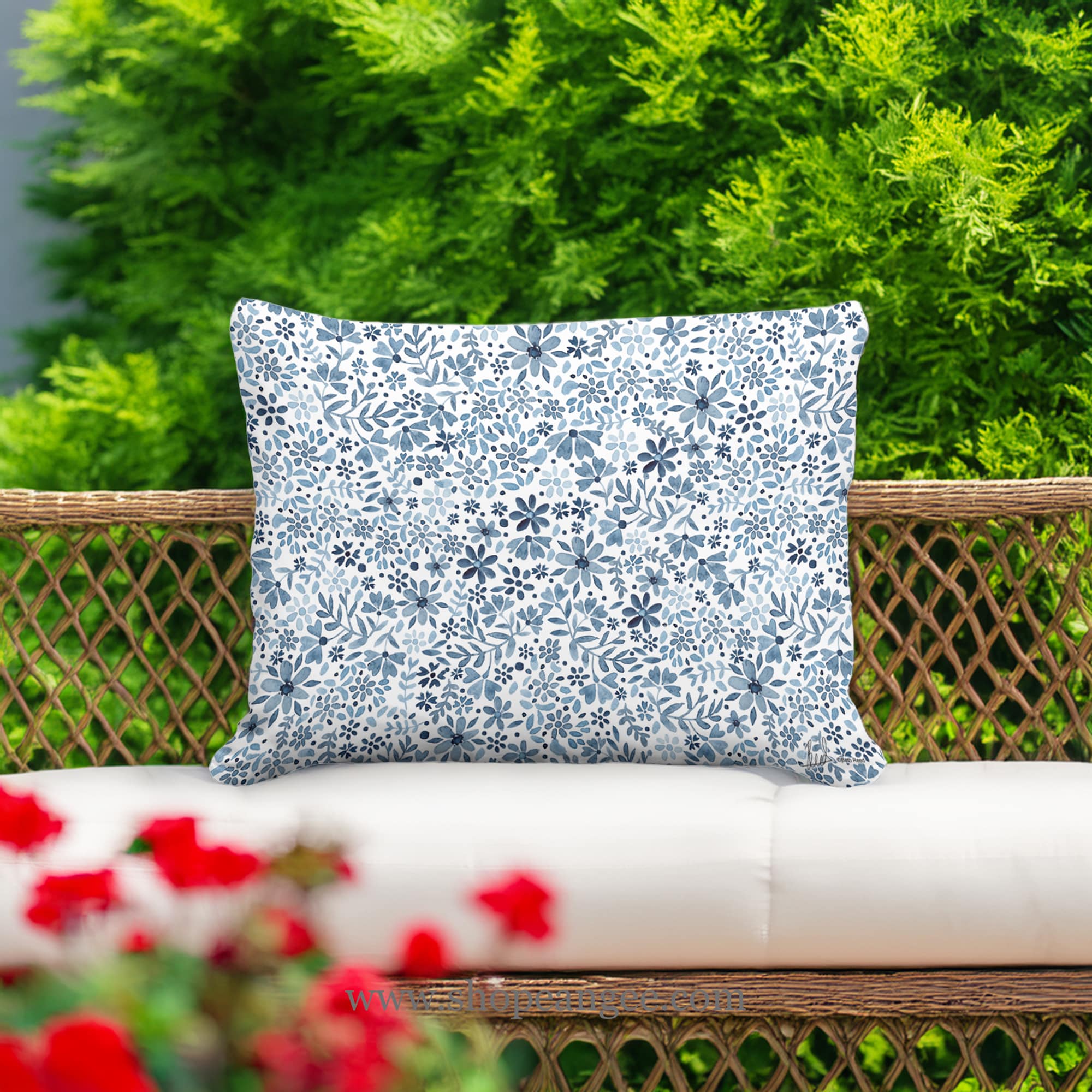 In an outdoor reading nook a multi colored outdoor pillow crafted by the artisans of Magnolia Casual called the Outdoor Pillow Indigo Flourish 19x24 is displayed featuring quality outdoor fabric adding comfort and style to the space.