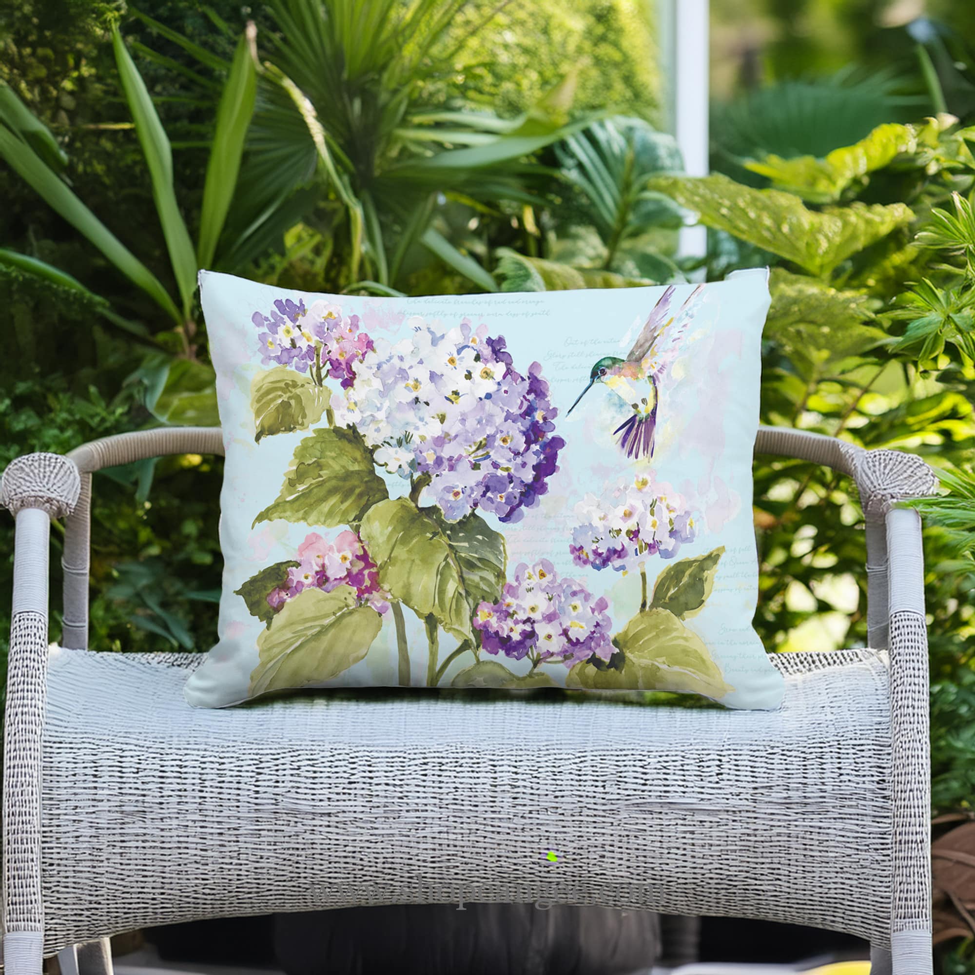 In a coastal inspired deck chair a multi colored outdoor pillow crafted by the artisans of Magnolia Casual called the Outdoor Pillow Hummingbird with Hydrangea 19x24 is displayed featuring handwoven textile adding comfort and style to the space featuring with a hummingbird motif.