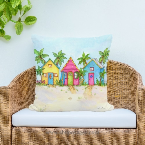 In a coastal inspired deck chair a multi colored outdoor pillow crafted by the artisans of Magnolia Casual called the Outdoor Pillow Colorful Beach Cottages 18x18 is displayed featuring quality outdoor fabric, eco friendly adding comfort and style to the space.