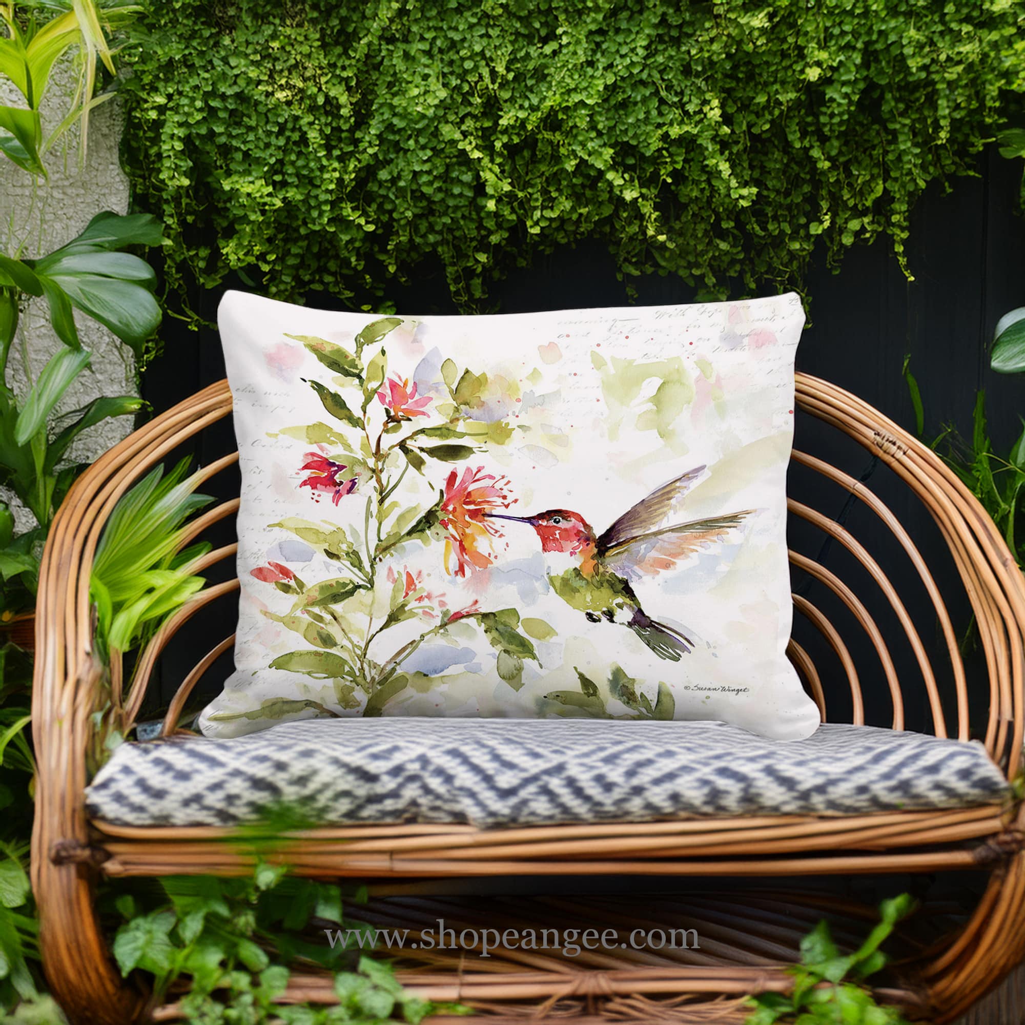 In a sunlit patio lounge a multi colored outdoor pillow crafted by the artisans of Magnolia Casual called the Outdoor Pillow Hummer with Hanging Plant 2 13x18 is displayed featuring quality outdoor fabric adding comfort and style to the space.