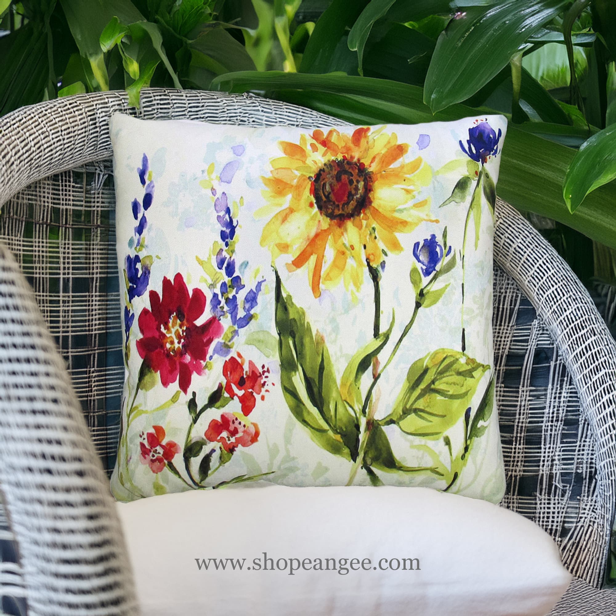 In a cozy garden seating area a multi colored outdoor pillow crafted by the artisans of Magnolia Casual called the Outdoor Pillow Sunflower Field 18X18 is displayed featuring handwoven textile adding comfort and style to the space featuring with a sunflower motif.