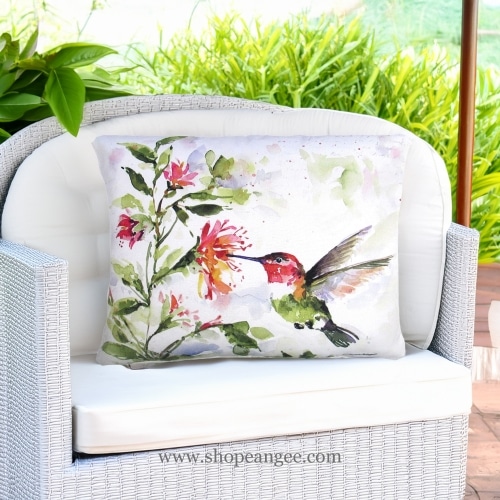 In a poolside chaise a multi colored outdoor pillow crafted by the artisans of Magnolia Casual called the Outdoor Pillow Hummer w/Hanging Plant 2 19x24 is displayed featuring quality outdoor fabric adding comfort and style to the space.