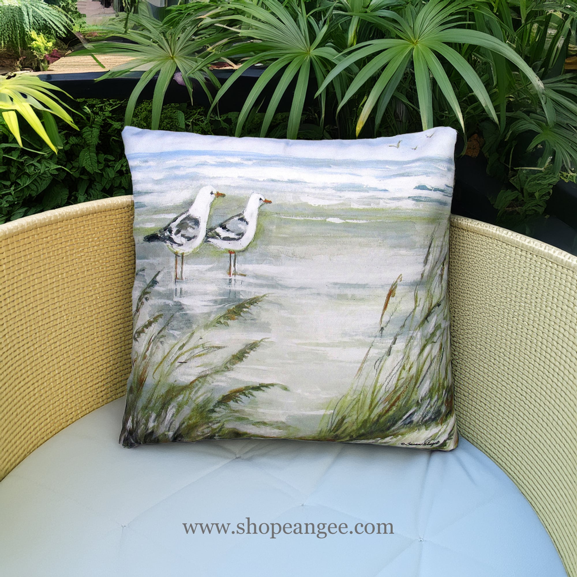 In a sunlit patio lounge a multi colored outdoor pillow crafted by the artisans of Magnolia Casual called the Outdoor Pillow Seagulls on Beach 18x18 is displayed featuring quality outdoor fabric adding comfort and style to the space.