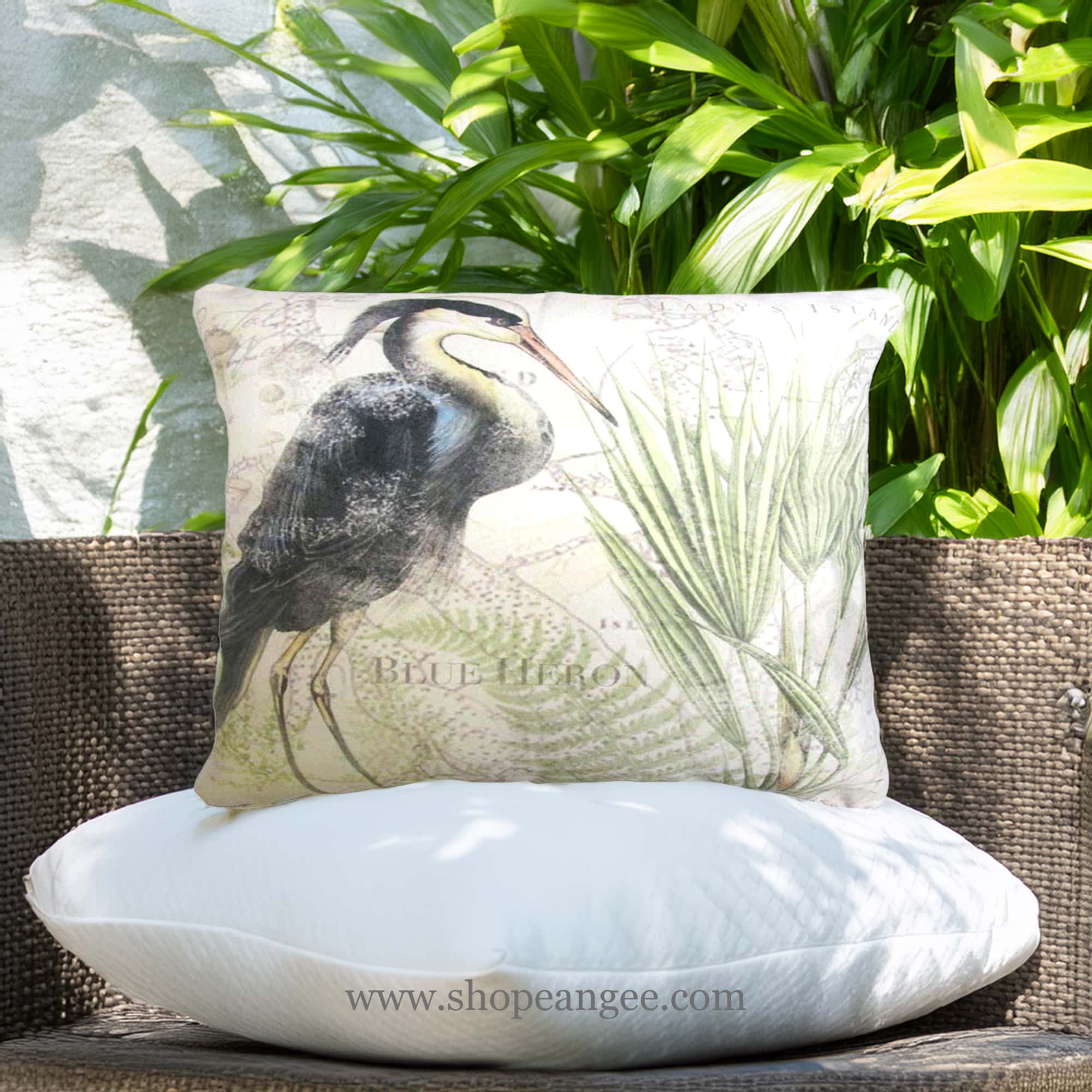 In an outdoor reading nook a multi colored outdoor pillow crafted by the artisans of Magnolia Casual called the Outdoor Pillow Great Heron 1 19x24 is displayed featuring quality outdoor fabric, natural materials adding comfort and style to the space.