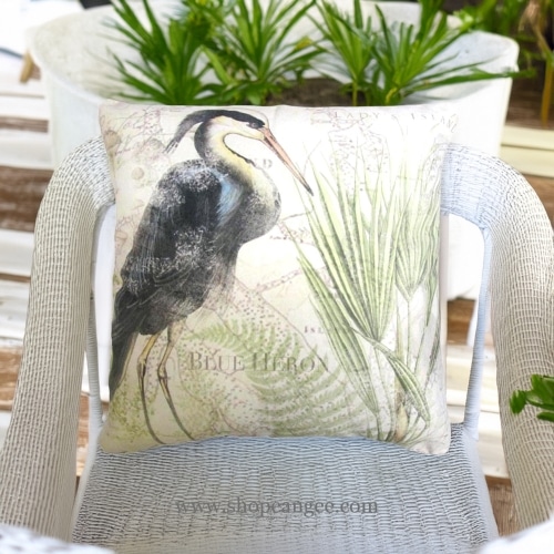 In a cozy garden seating area a multi colored outdoor pillow crafted by the artisans of Magnolia Casual called the Outdoor Pillow Great Heron 1 18x18 is displayed featuring quality outdoor fabric, natural materials adding comfort and style to the space.