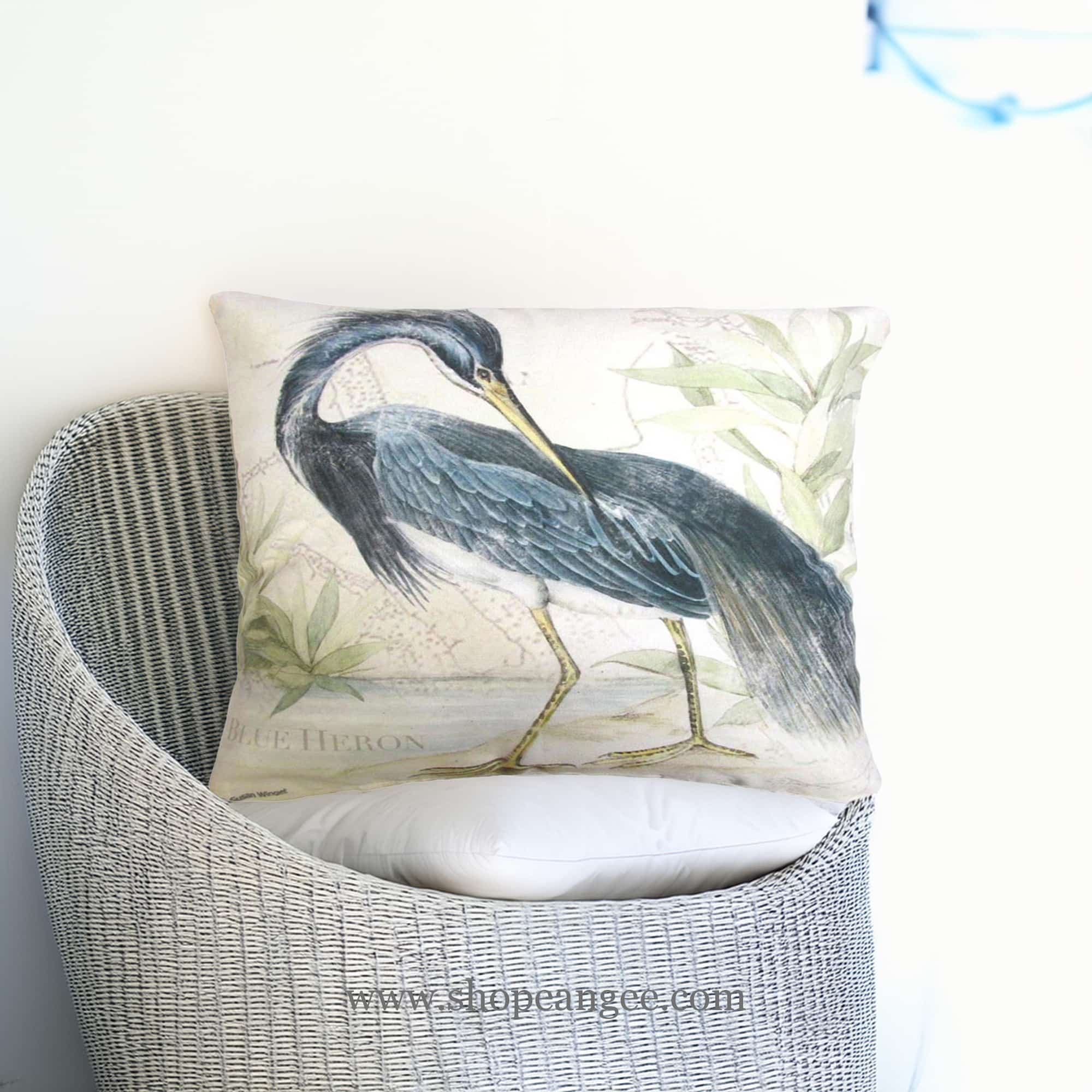 In an outdoor reading nook a multi colored outdoor pillow crafted by the artisans of Magnolia Casual called the Outdoor Pillow Great Heron 2 19x24 is displayed featuring quality outdoor fabric, natural materials adding comfort and style to the space.