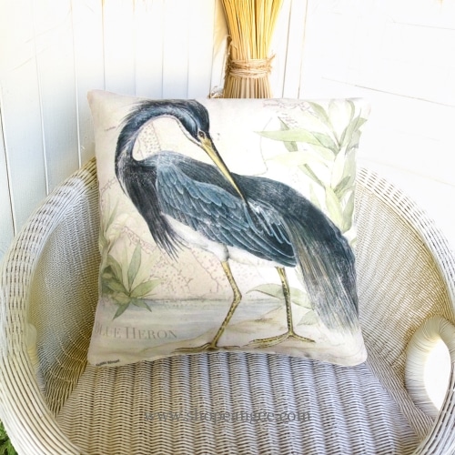 In a shaded porch swing a multi colored outdoor pillow crafted by the artisans of Magnolia Casual called the Outdoor Pillow Great Heron 2 18x18 is displayed featuring quality outdoor fabric, natural materials adding comfort and style to the space.