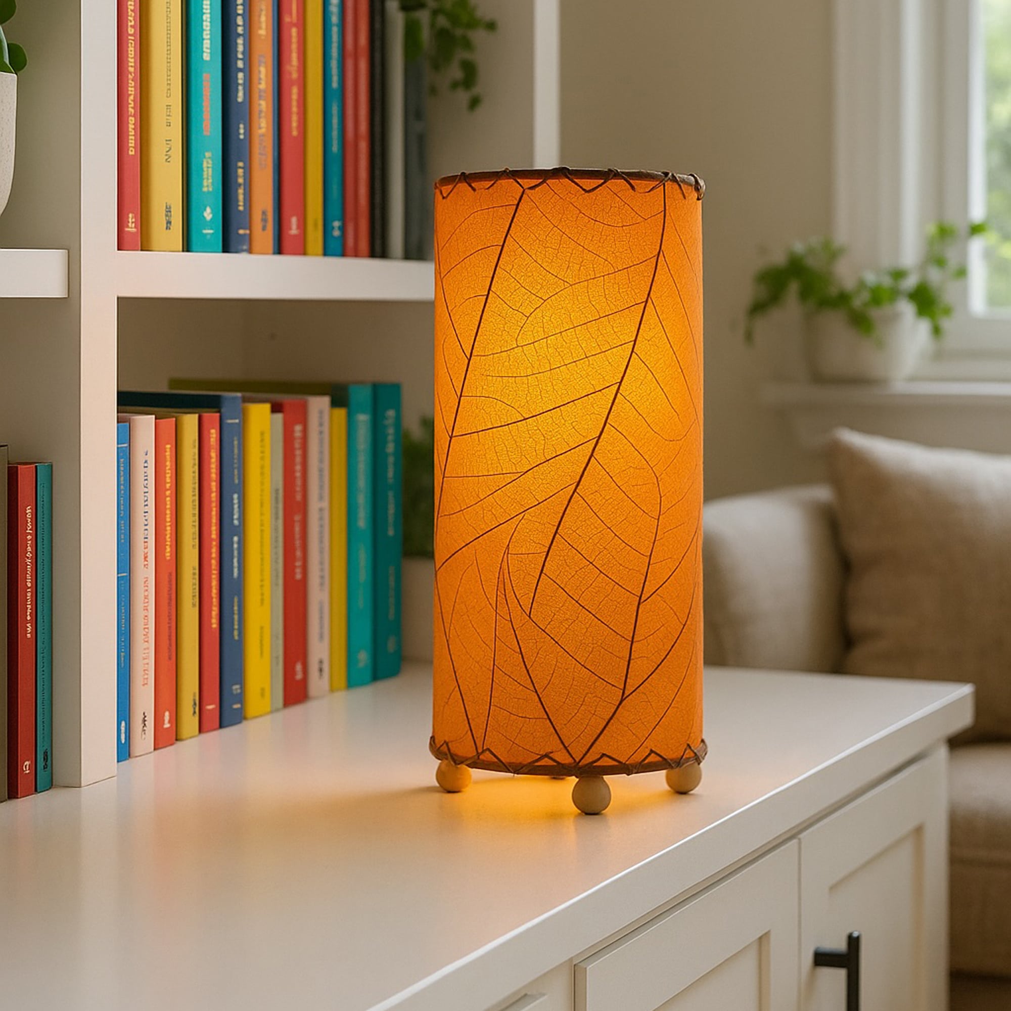 Eco-friendly orange cylinder table lamp by Eangee, set on a white shelf surrounded by colorful books in a cozy living space.