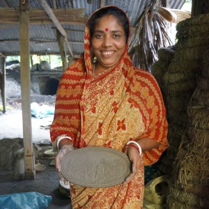 Artisan in Bangladesh holding a freshly crafted terracotta bread warmer plate before firing, part of the traditional pottery process that connects global bread making history.