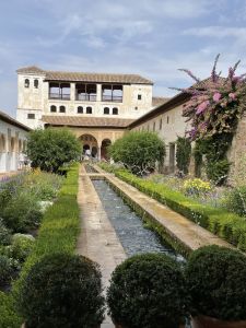 Historic courtyard garden at the Alhambra with water channel, fountains, flowering plants, shaded architecture, and natural materials